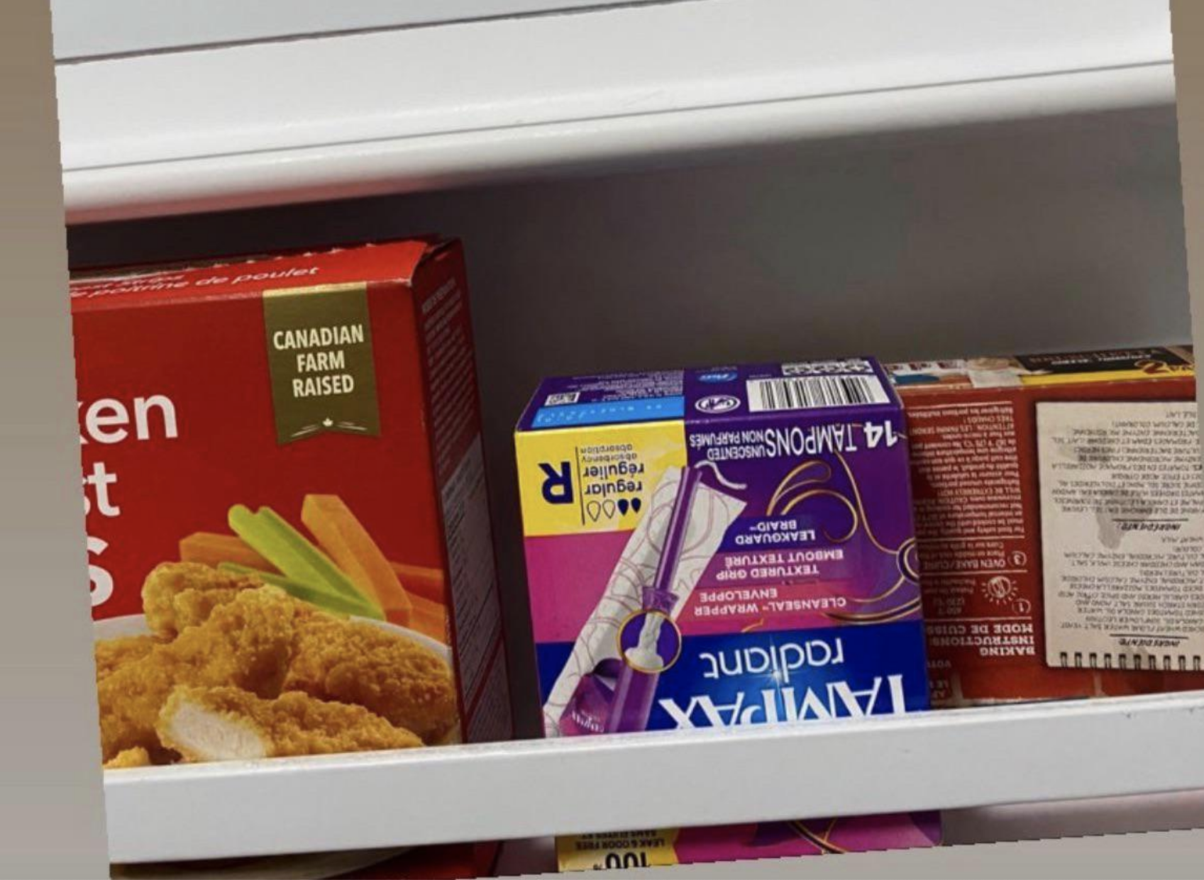 A box of tampons has been put upside down in the freezer next to boxed dinners and lunches