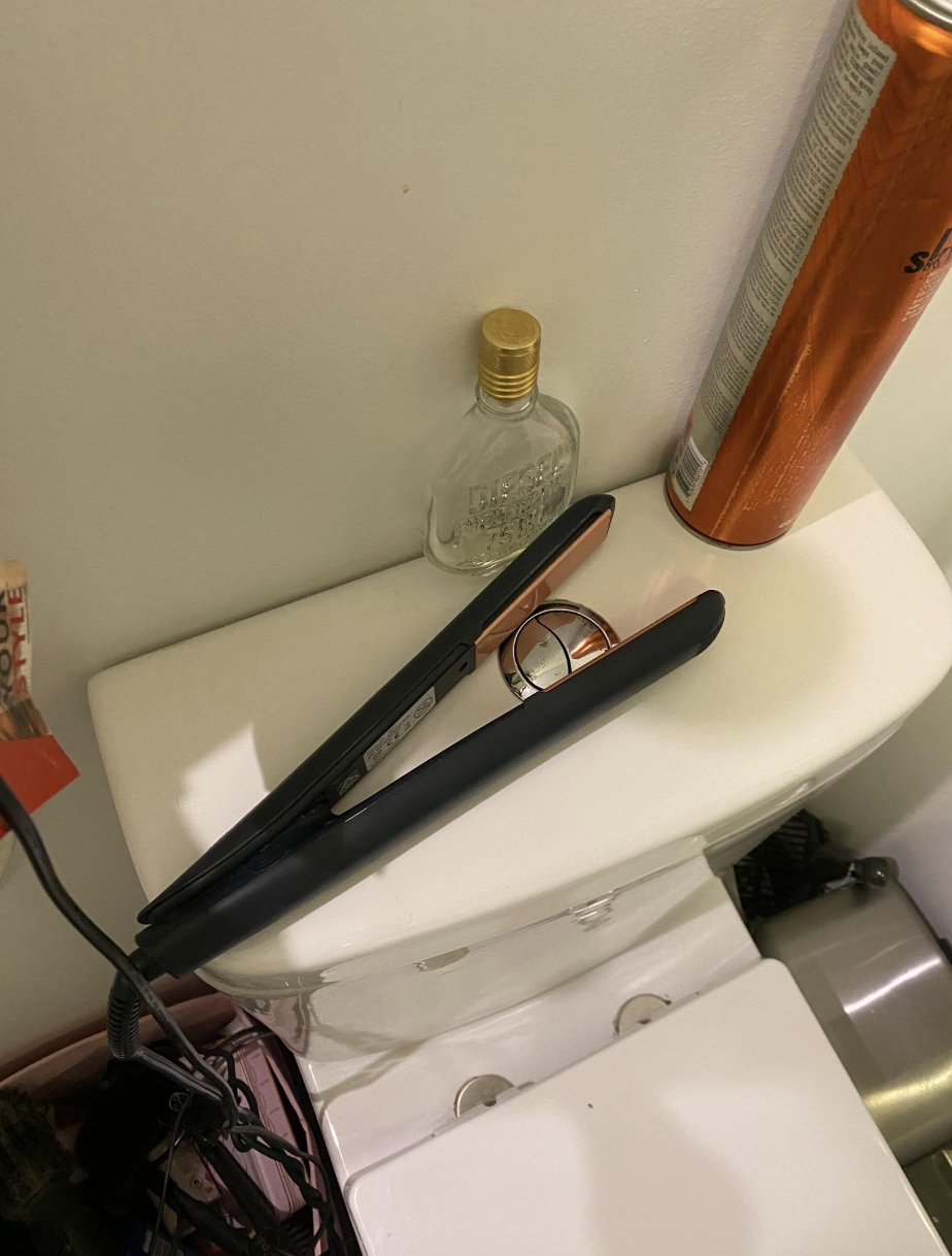 A hot curling iron has been placed so that it&#x27;s surrounding the button on top of the toilet that has to be pressed to flush it
