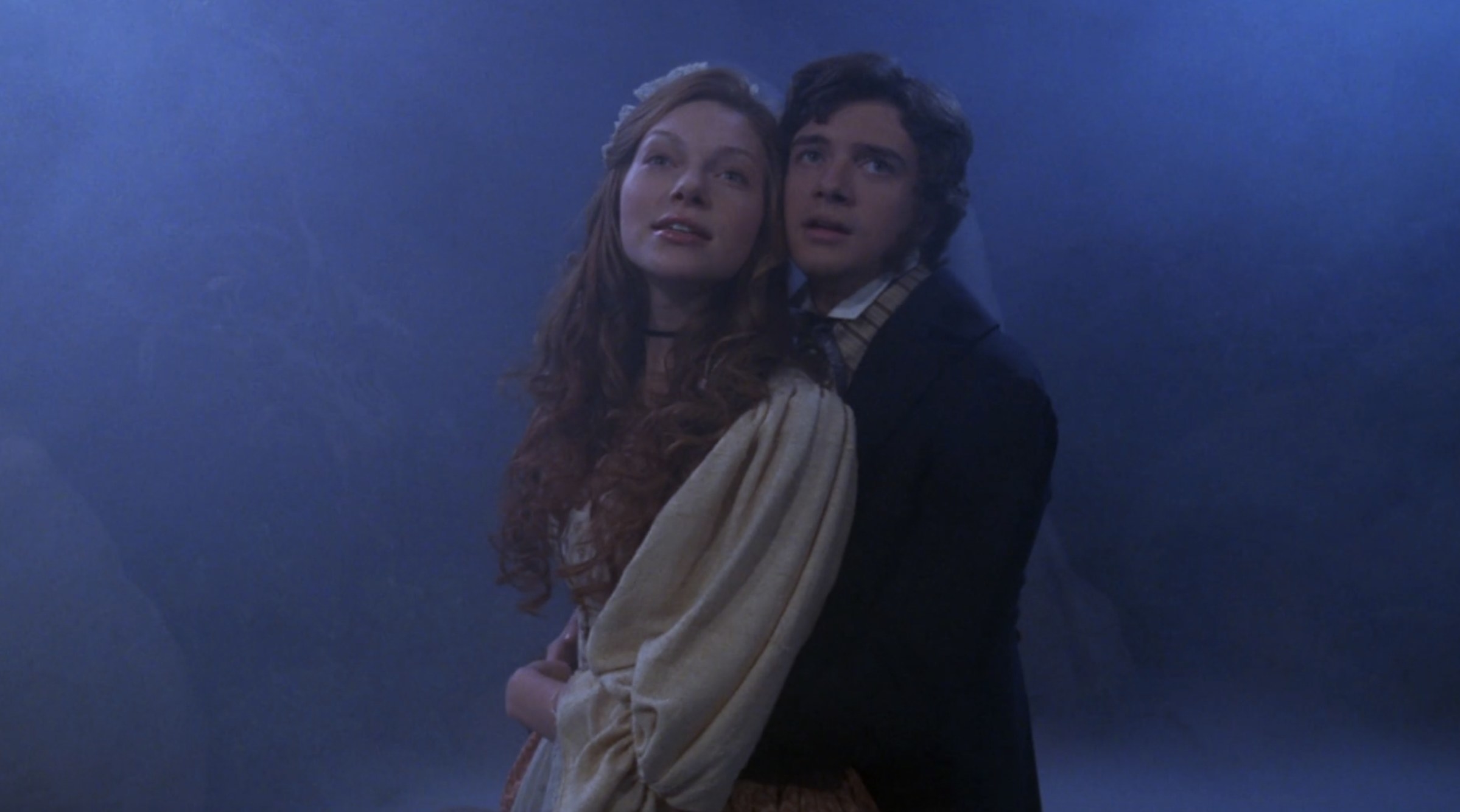 Eric and Donna re dressed as a 19th century romance hero and heroine, he holds her from behind