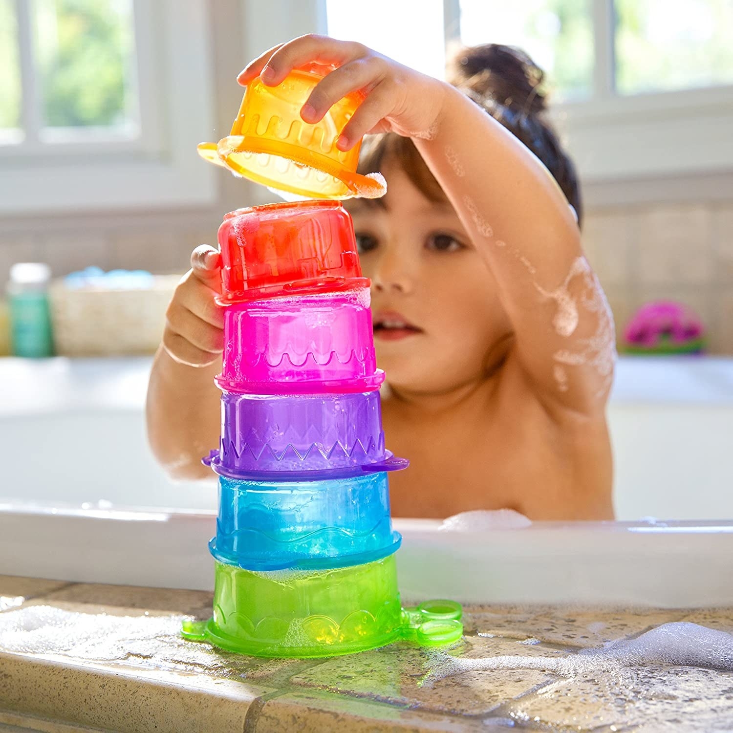 A kid stacking the cups on the edge of a bath