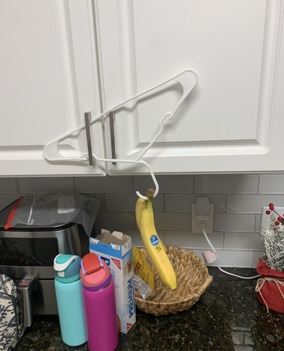 The boyfriend has placed a clothes hanger upside down on the handle of a cabinet door and hung bananas from the hook that is meant to be used to hang up clothes