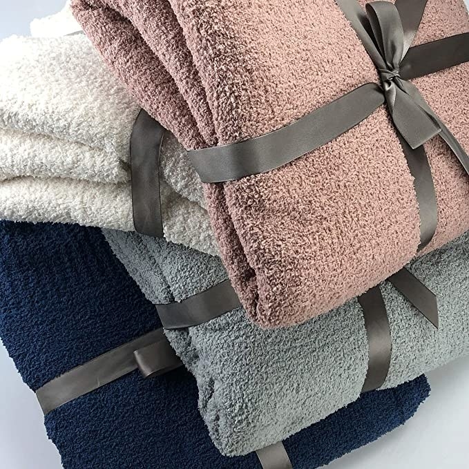 a pile of four blankets (white, pink, grey, and navy) wrapped in ribbons in a pile