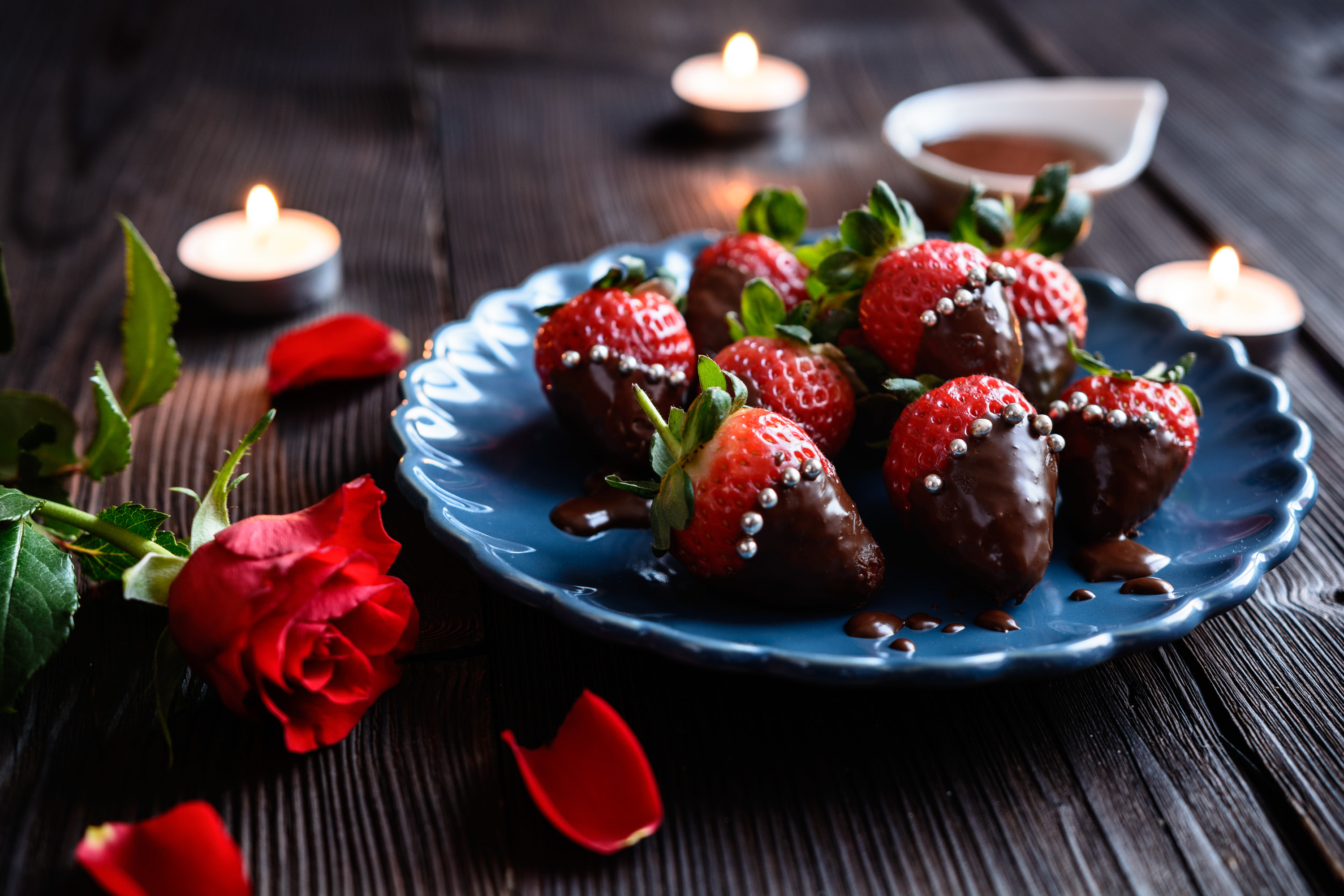 Roses, tea light candles and chocolate covered strawberries on a plate