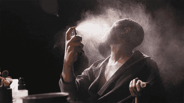 A GIF of man spraying himself with scent from a bottle