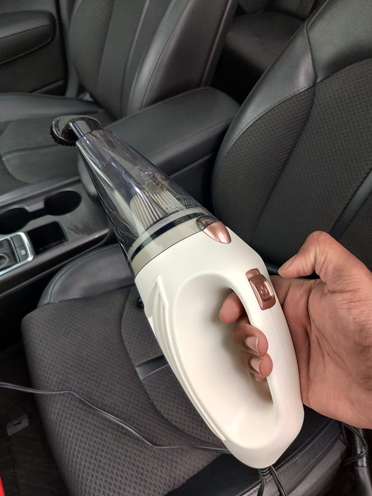 hand holding white portable car vacuum above gray carseat