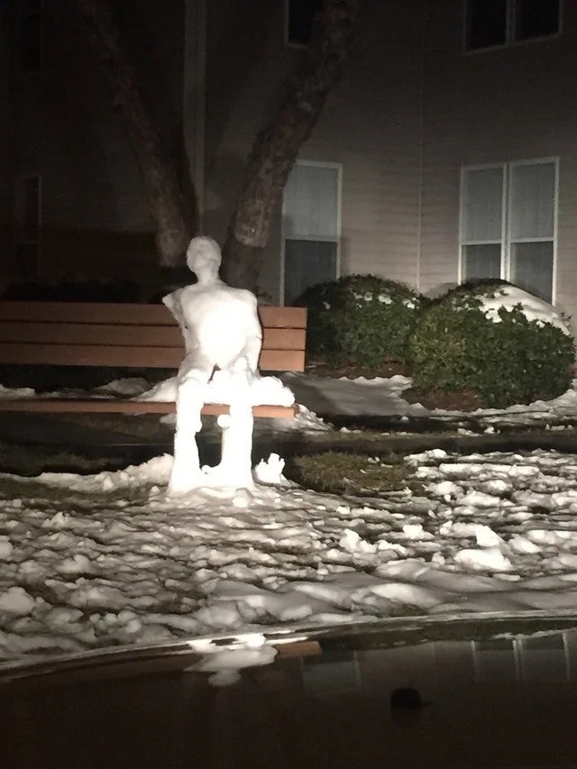 A very human-like snowman sitting on a bench