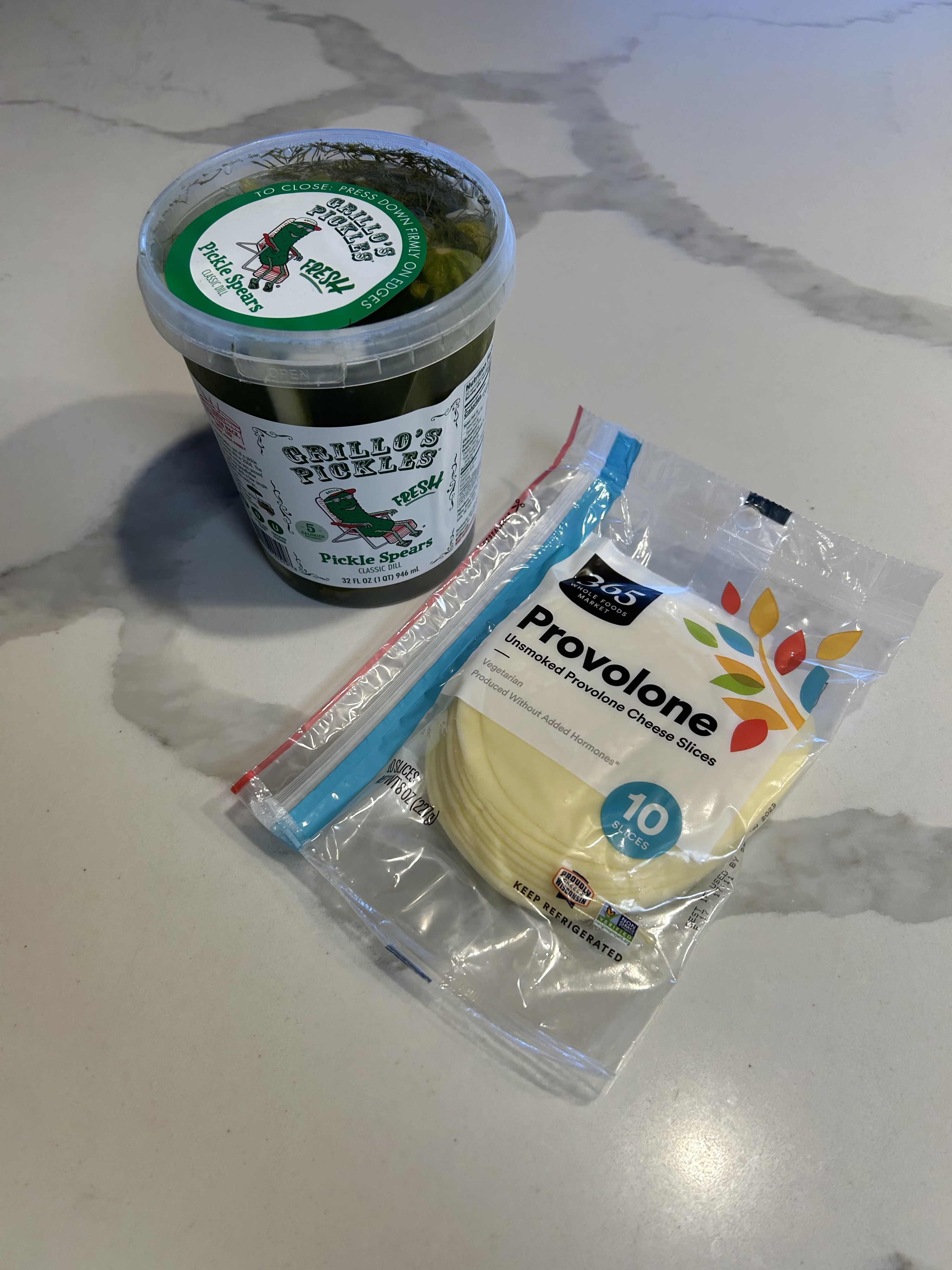 A container of pickles and a package of provolone on a kitchen counter