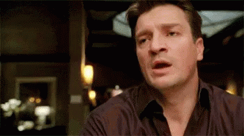 Nathan Fillion reaching out to interject in conversation then stopping, looking defeated
