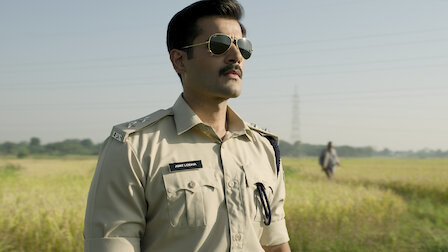 Karan Tacker, wearing sunglasses, is standing in a field