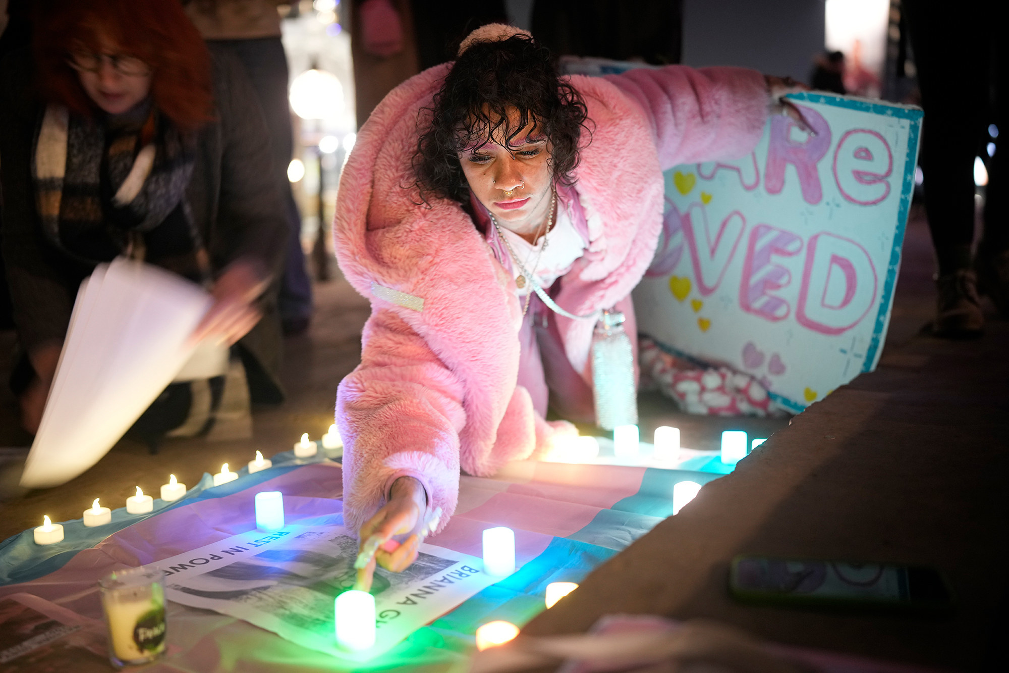 someone in a pink coat reaches for a candle at an outdoor candlelit vigil
