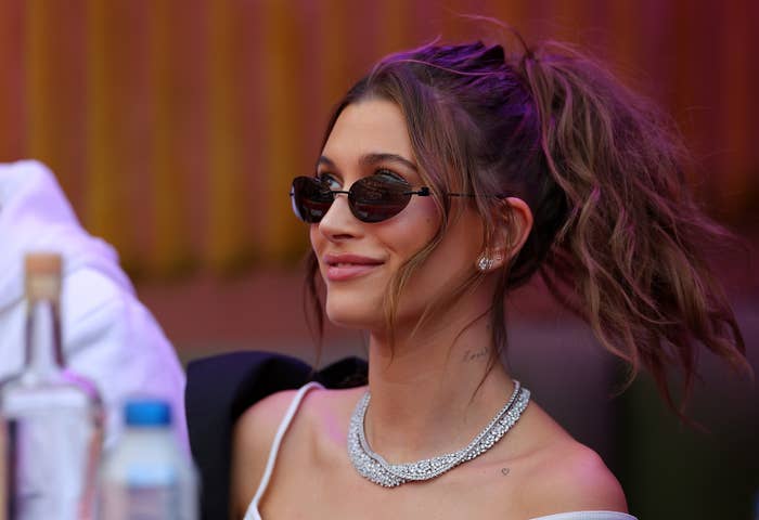 Hailey smiling as she looks up. She&#x27;s wearing sunglasses and a diamond necklace
