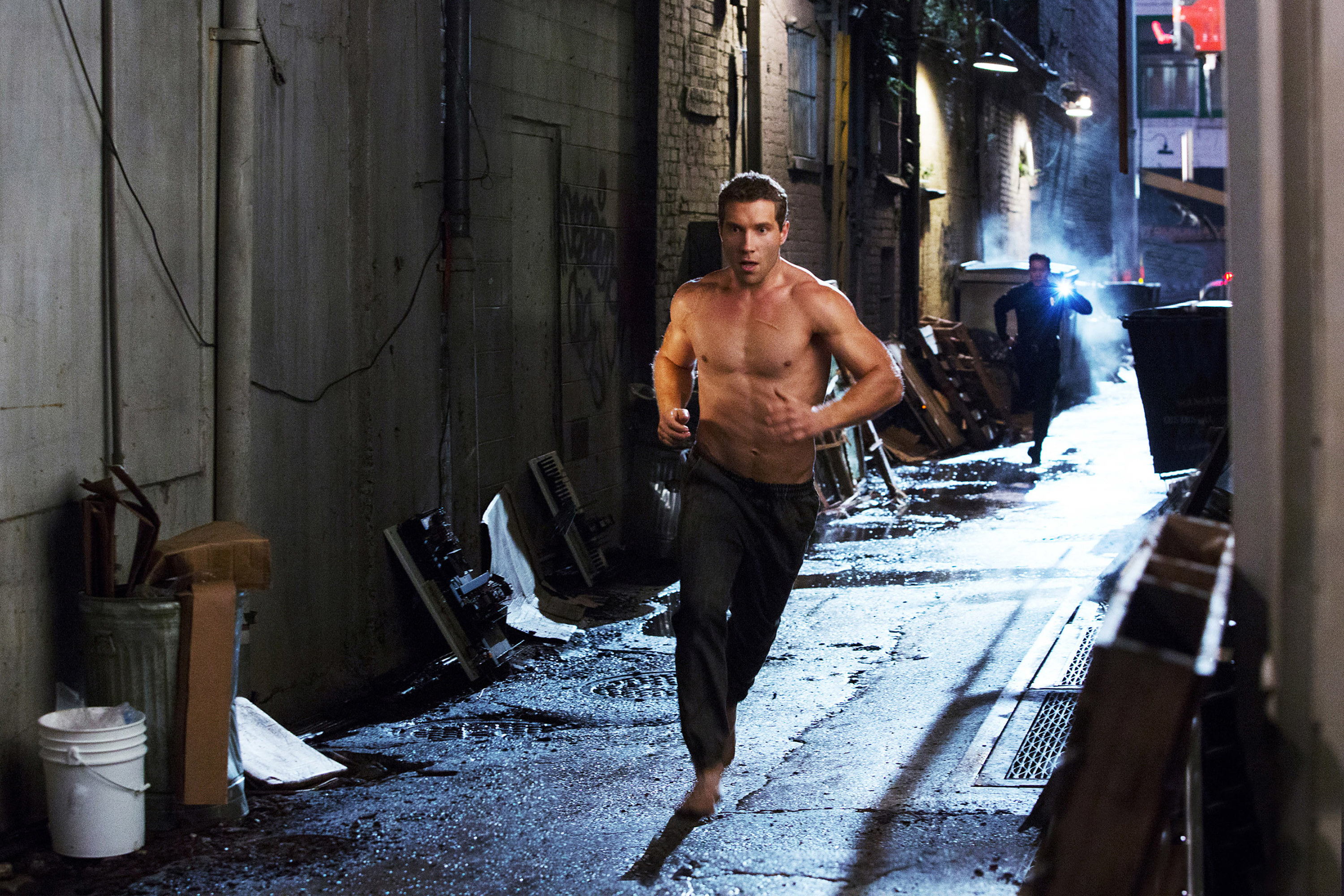 A shirtless man running down an alleyway