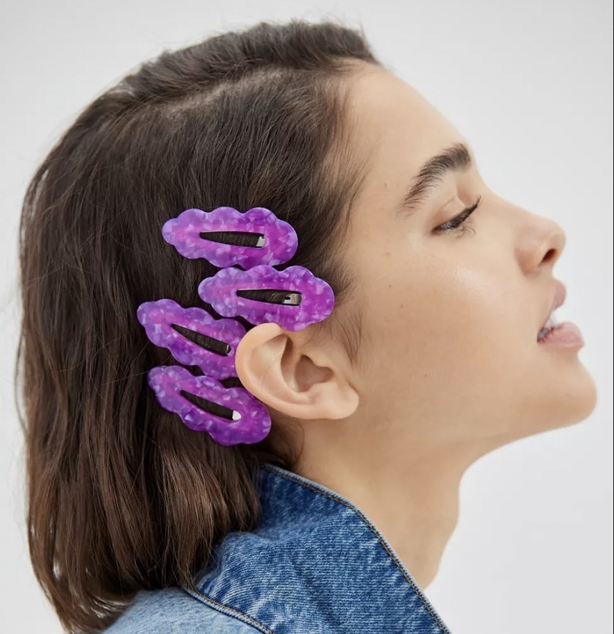 A person with short brown hair wearing four purple clips