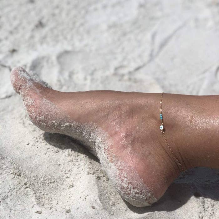 the anklet on someone&#x27;s foot that is covered in sand