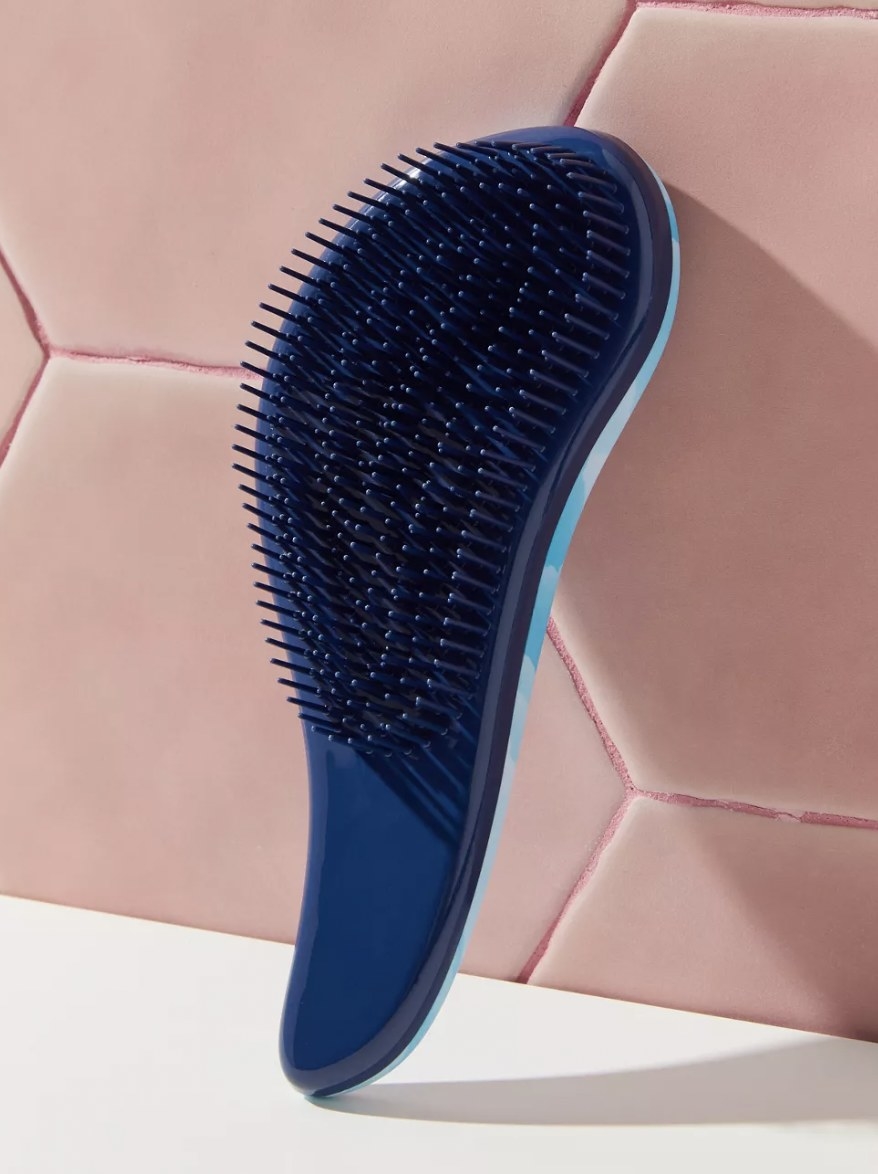 A blue detangling brush in front of pink tiles