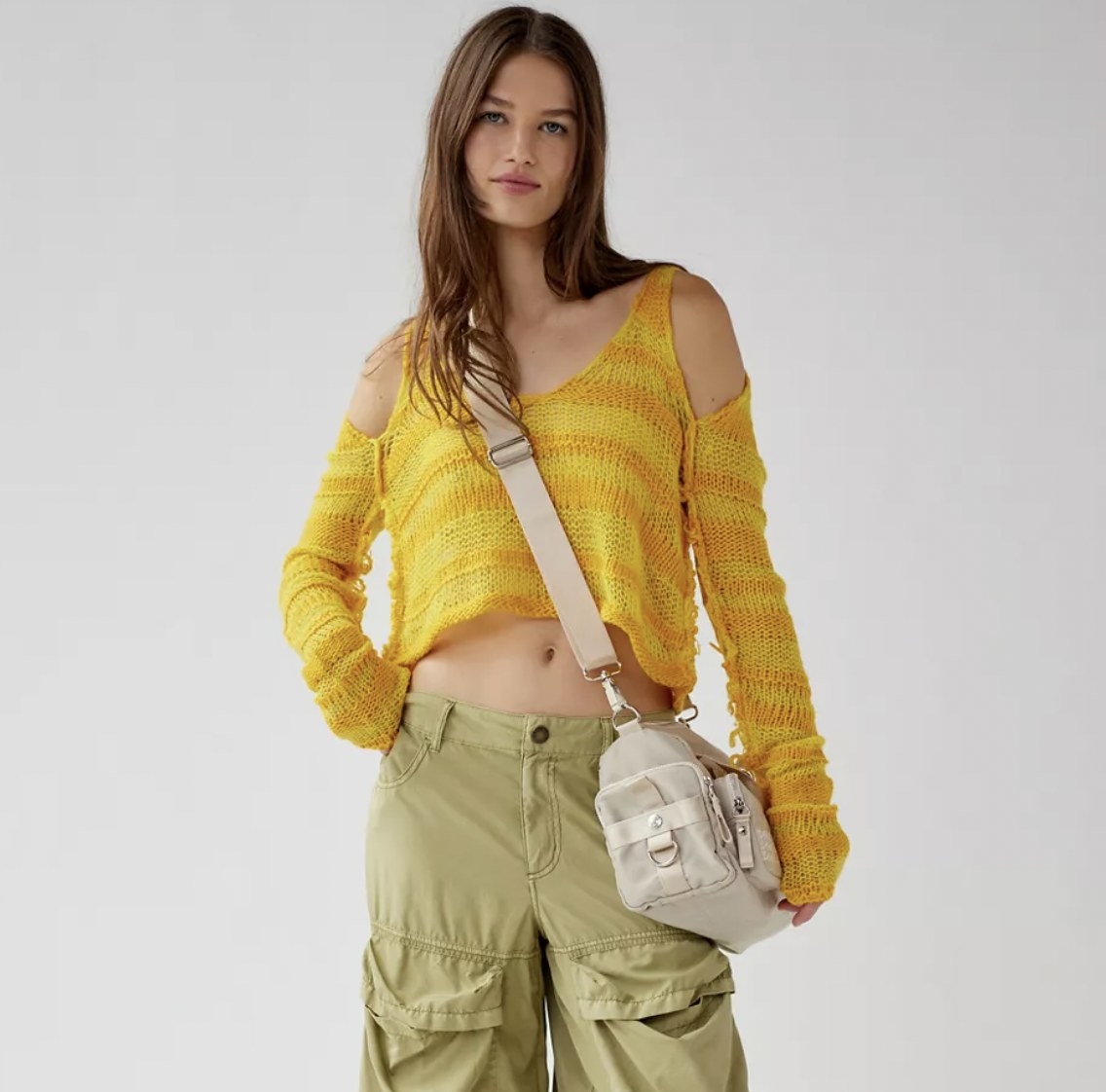 A person with long brown hair wearing a yellow striped cold-shoulder sweater