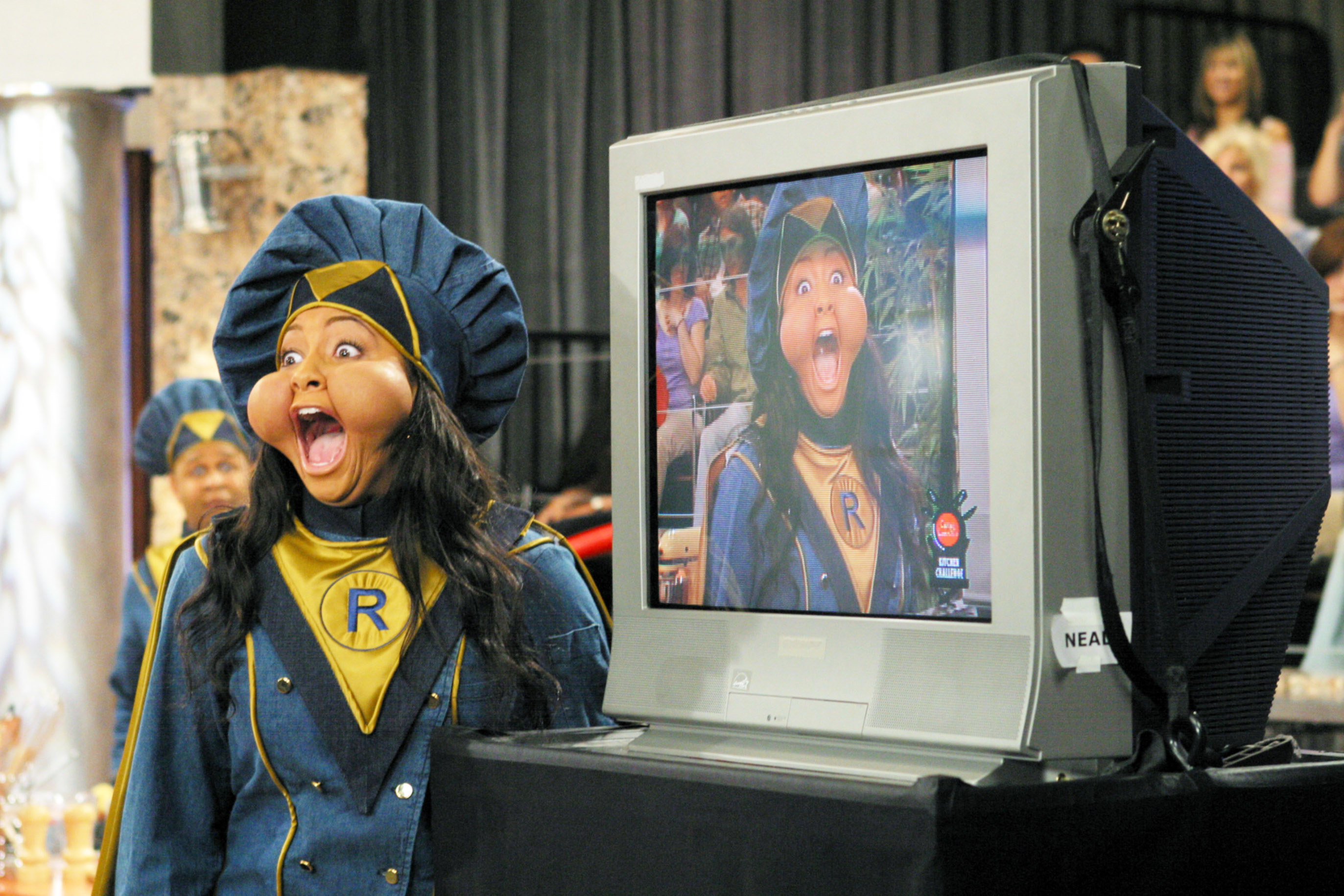 raven with huge cheeks standing next to a tv with her on it