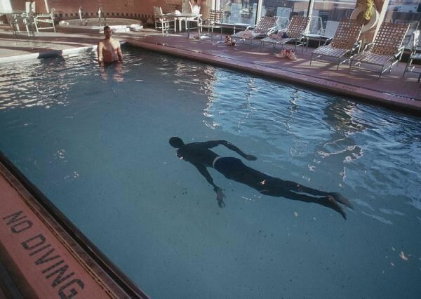 Manute Bol swimming in a pool, with his legs looking especially long
