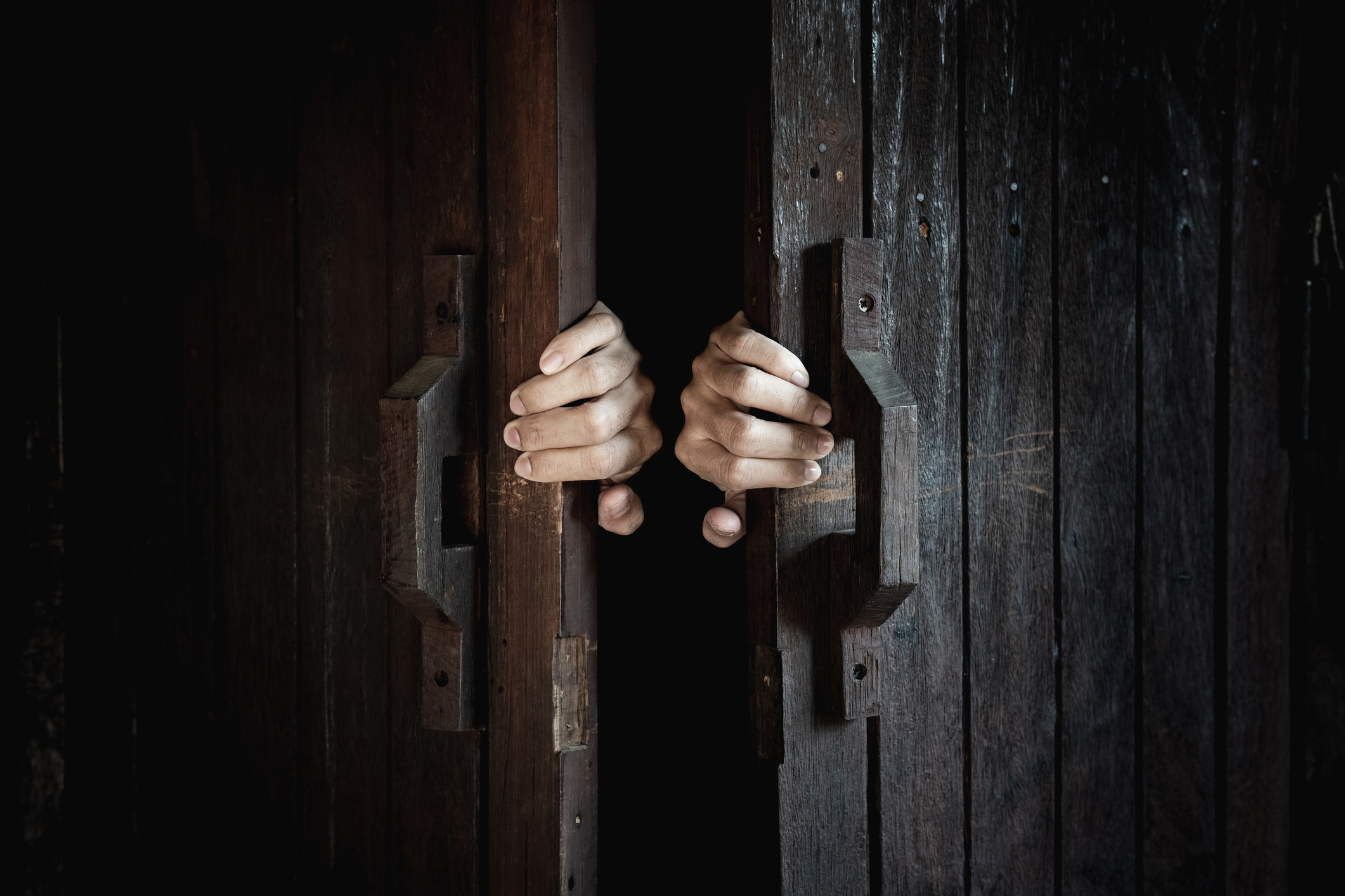 Hands open the wooden door from the inside of the dark room