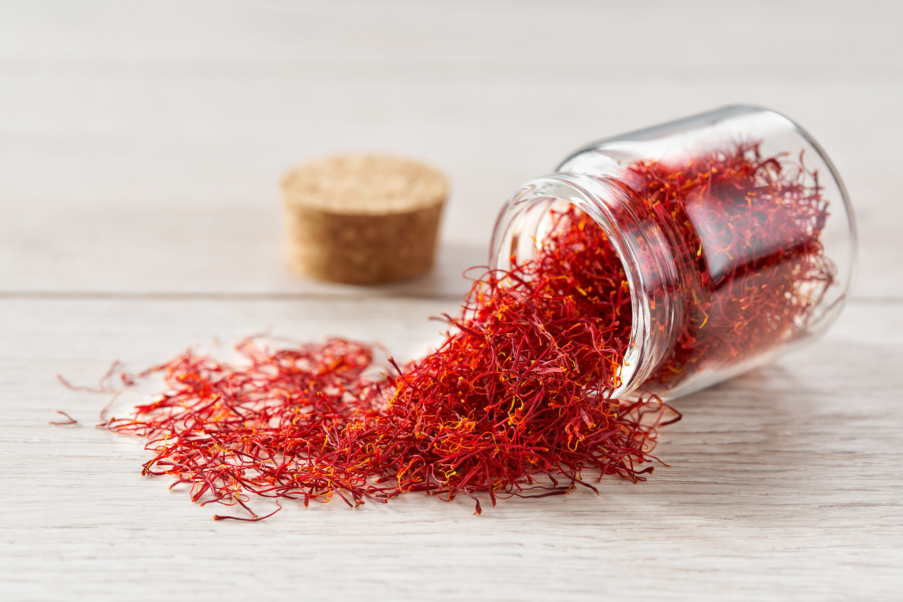 Saffron spill out of a glass storage jar on a wooden table
