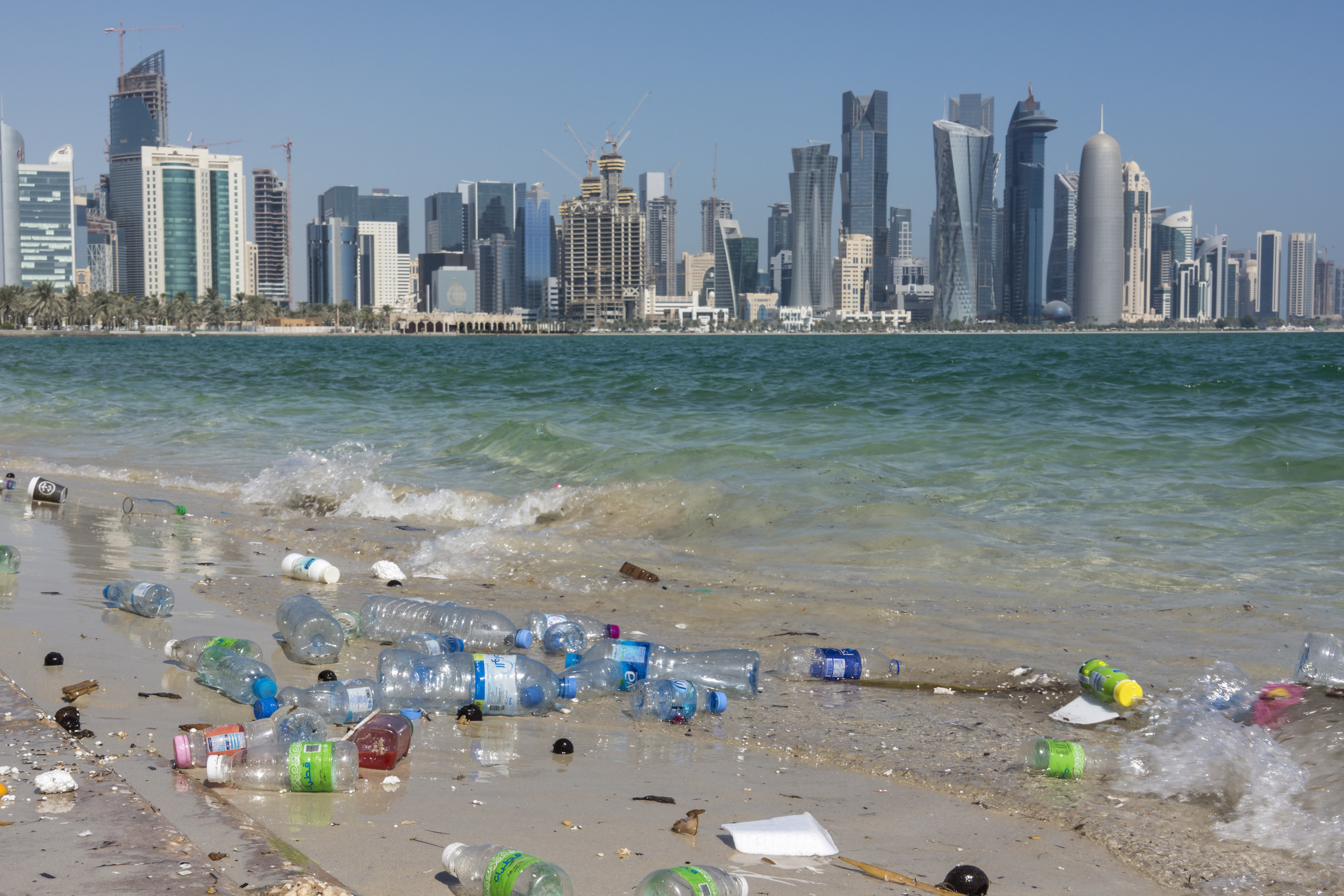 Plastic waste on the shore of the Arabian Gulf shows the problem of environmental pollution; in the background the modern skyline of Doha.