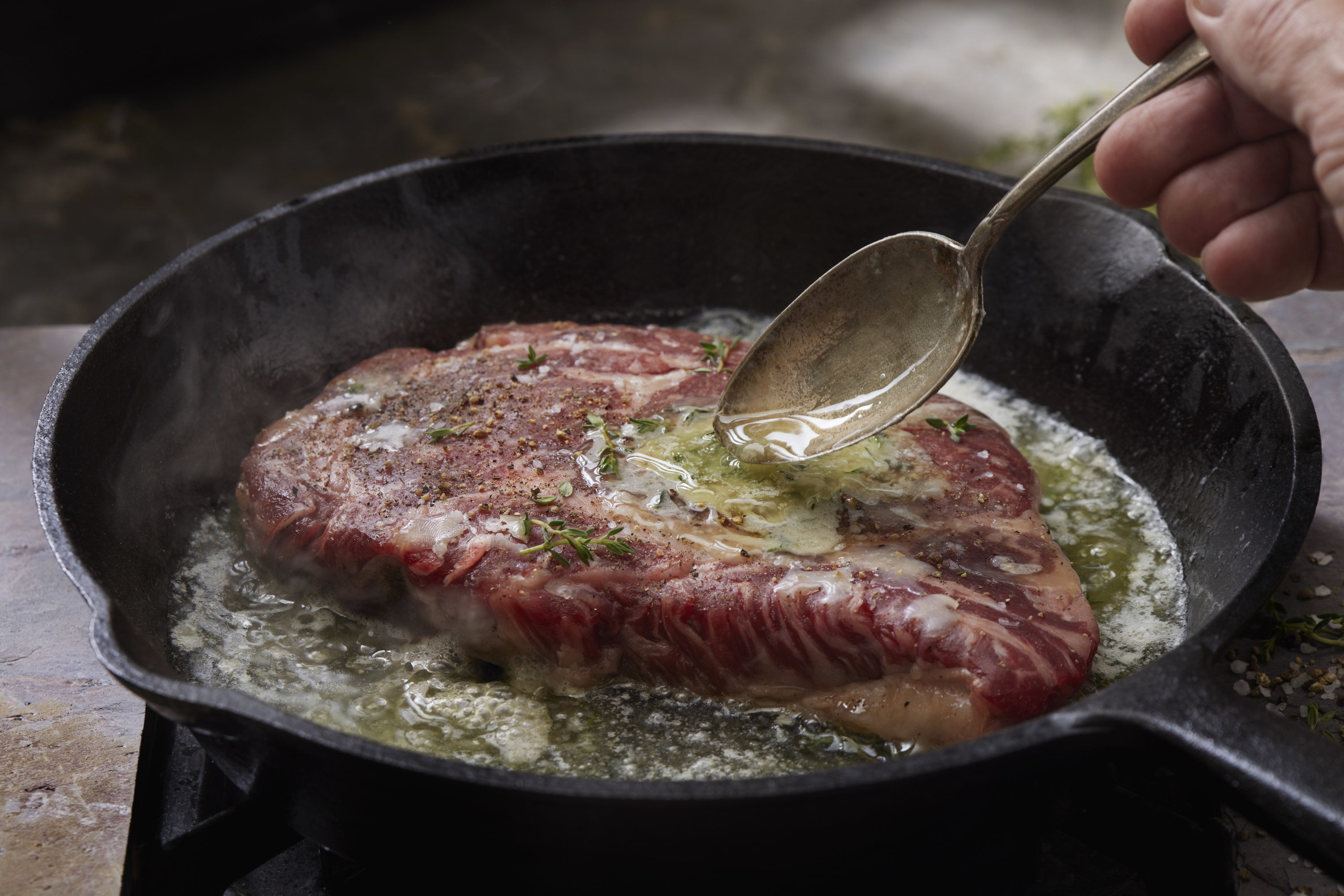 beef steak cooking in a pan with butter and herbs