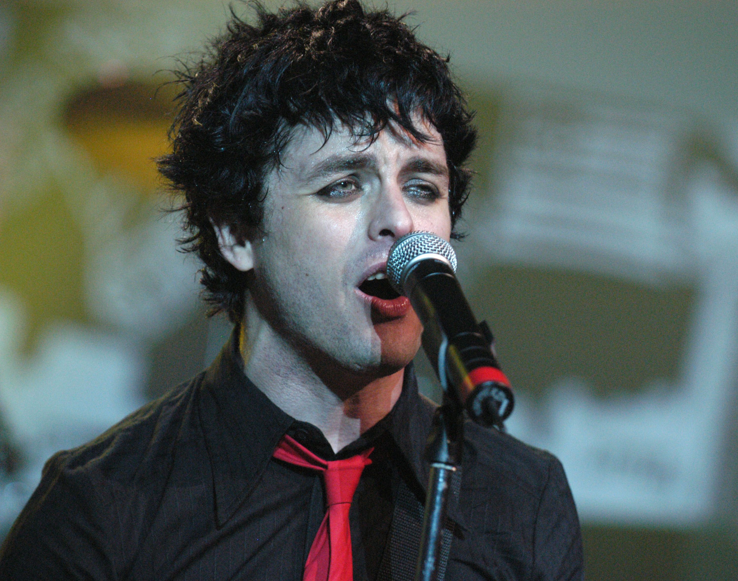 Billie Joe Armstrong performing on stage in a red tie