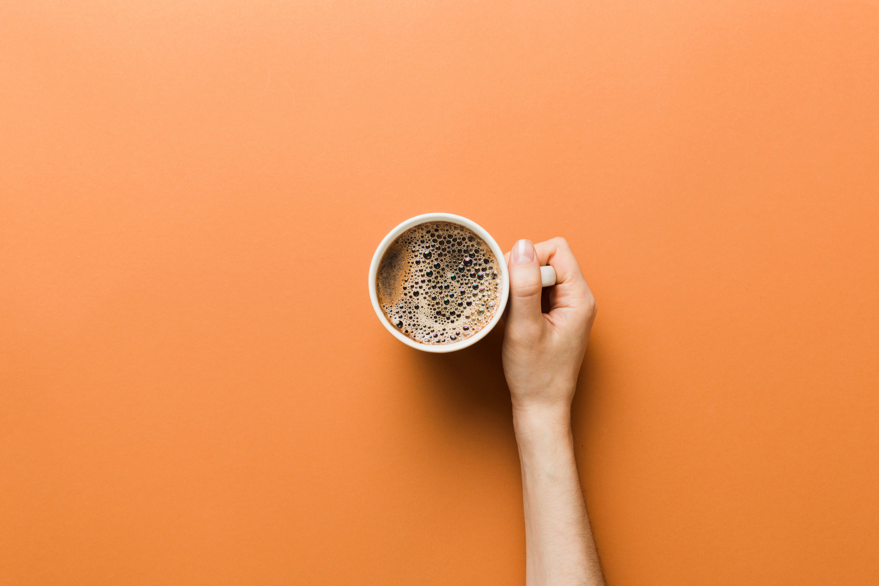 person holding a cup of coffee, shot from above with an orange background