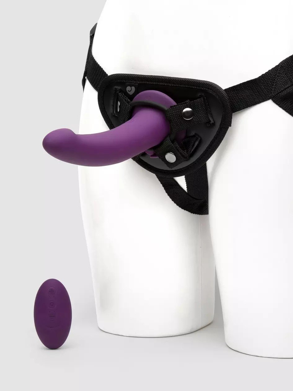 Mannequin wearing black harness with purple strap-on dildo and wireless remote
