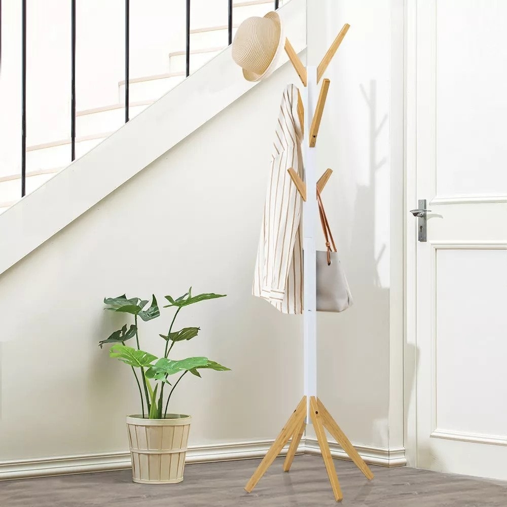 White and light wood coat rack with bag, shirt, and hat on it