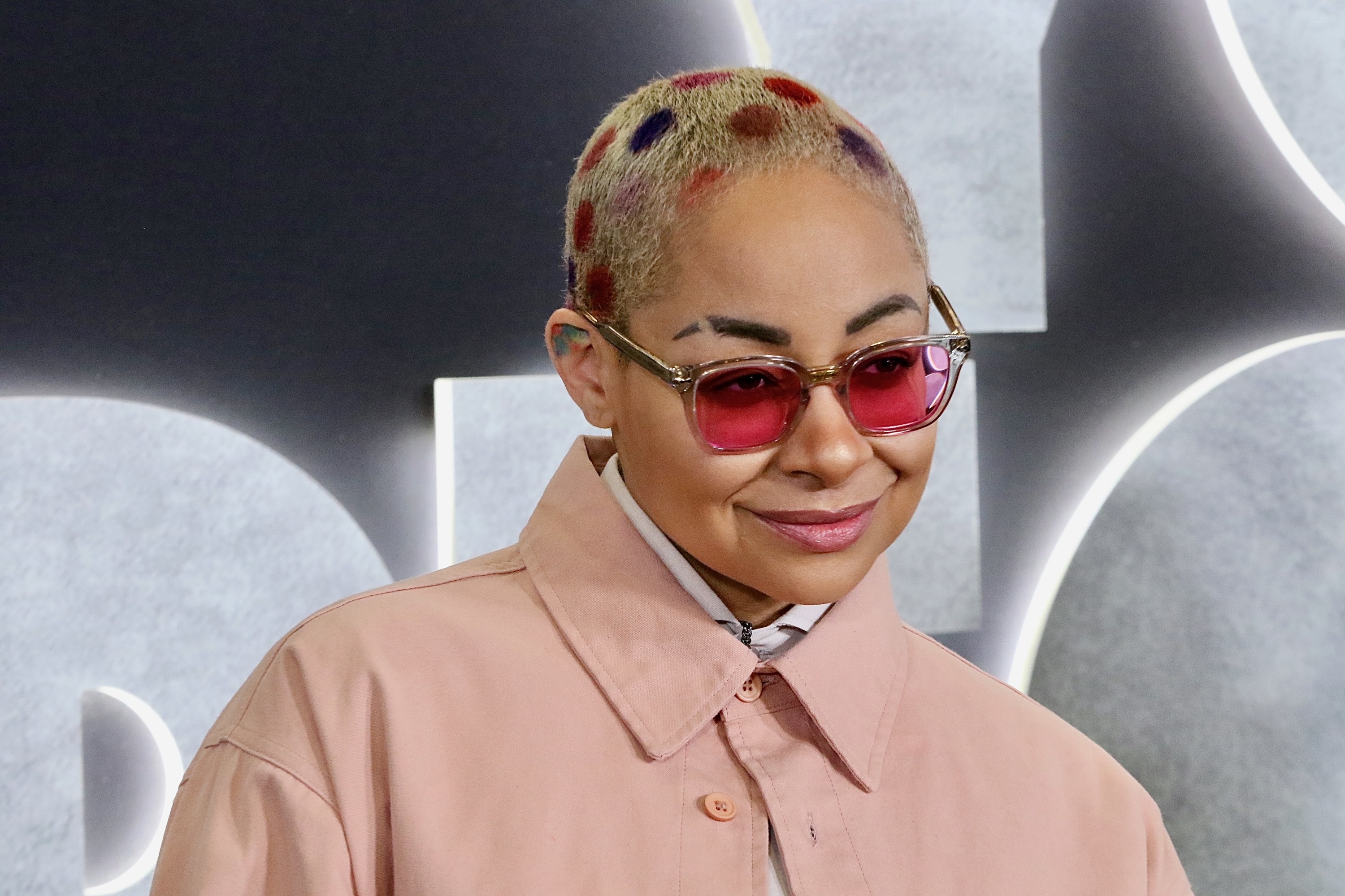 raven symone in a light pink jacket and red sunglasses
