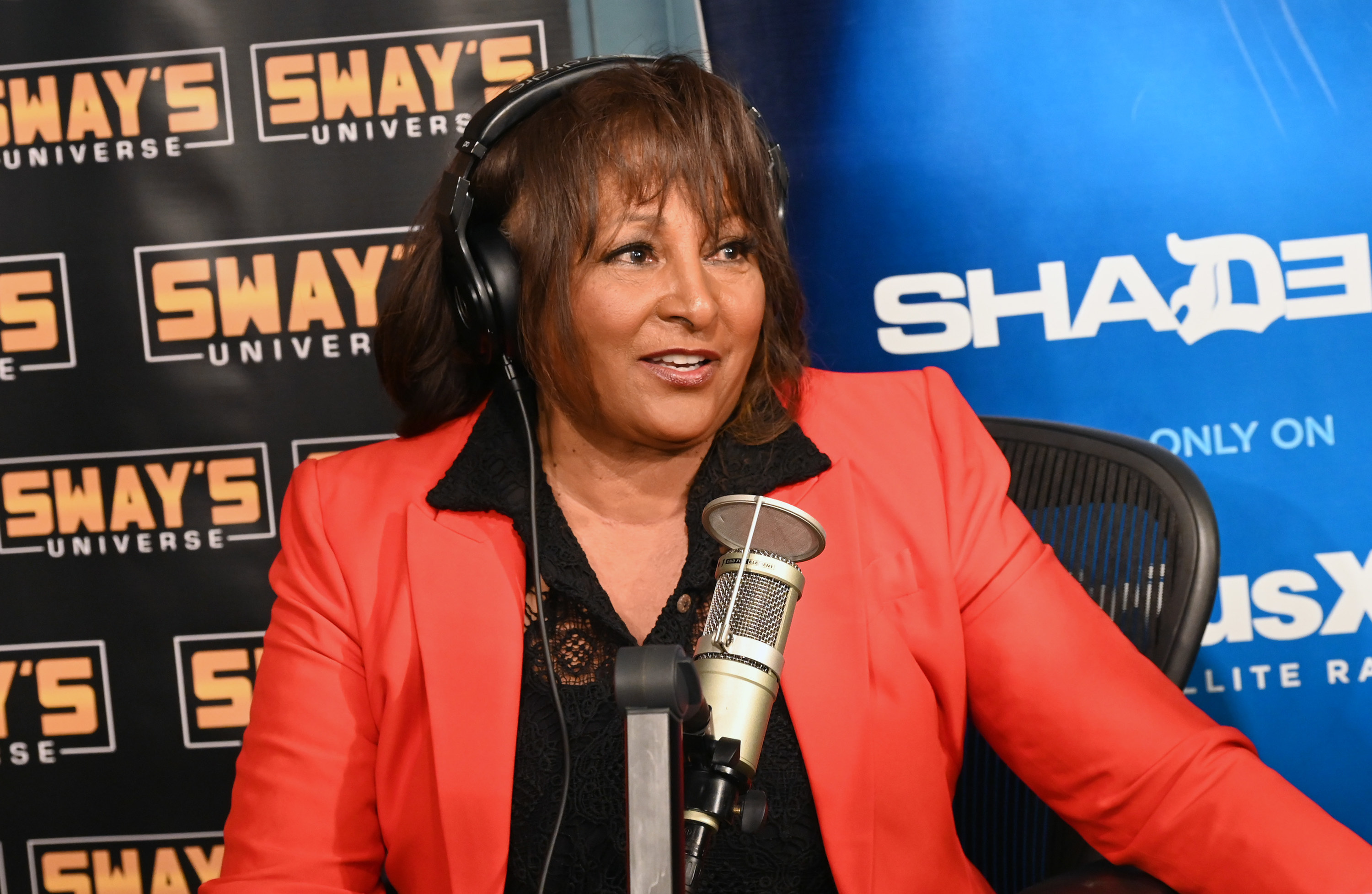 pam grier wearing a black shirt and orange blazer talking into a microphone