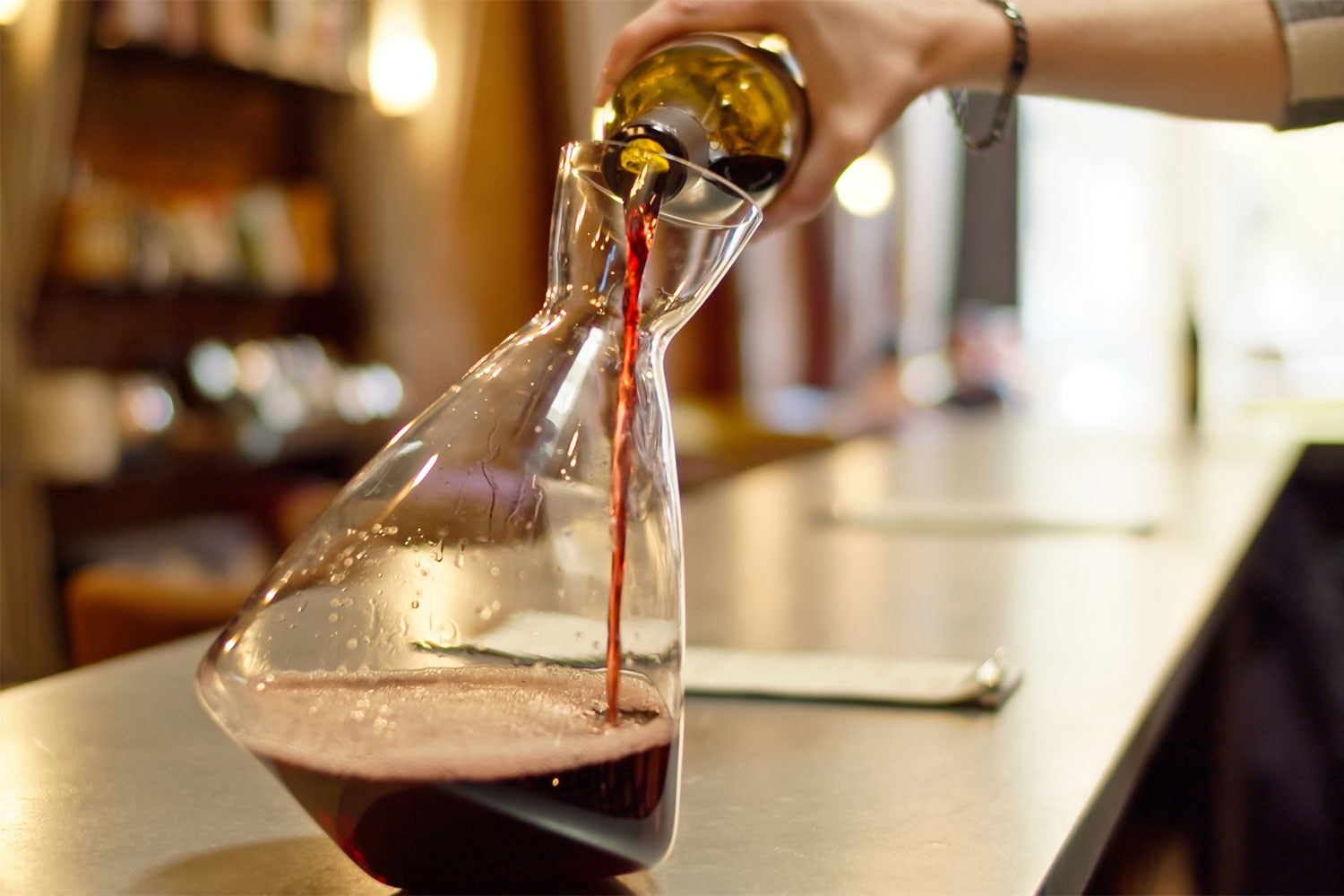 A sommelier pouring wine from a bottle into a decanter.