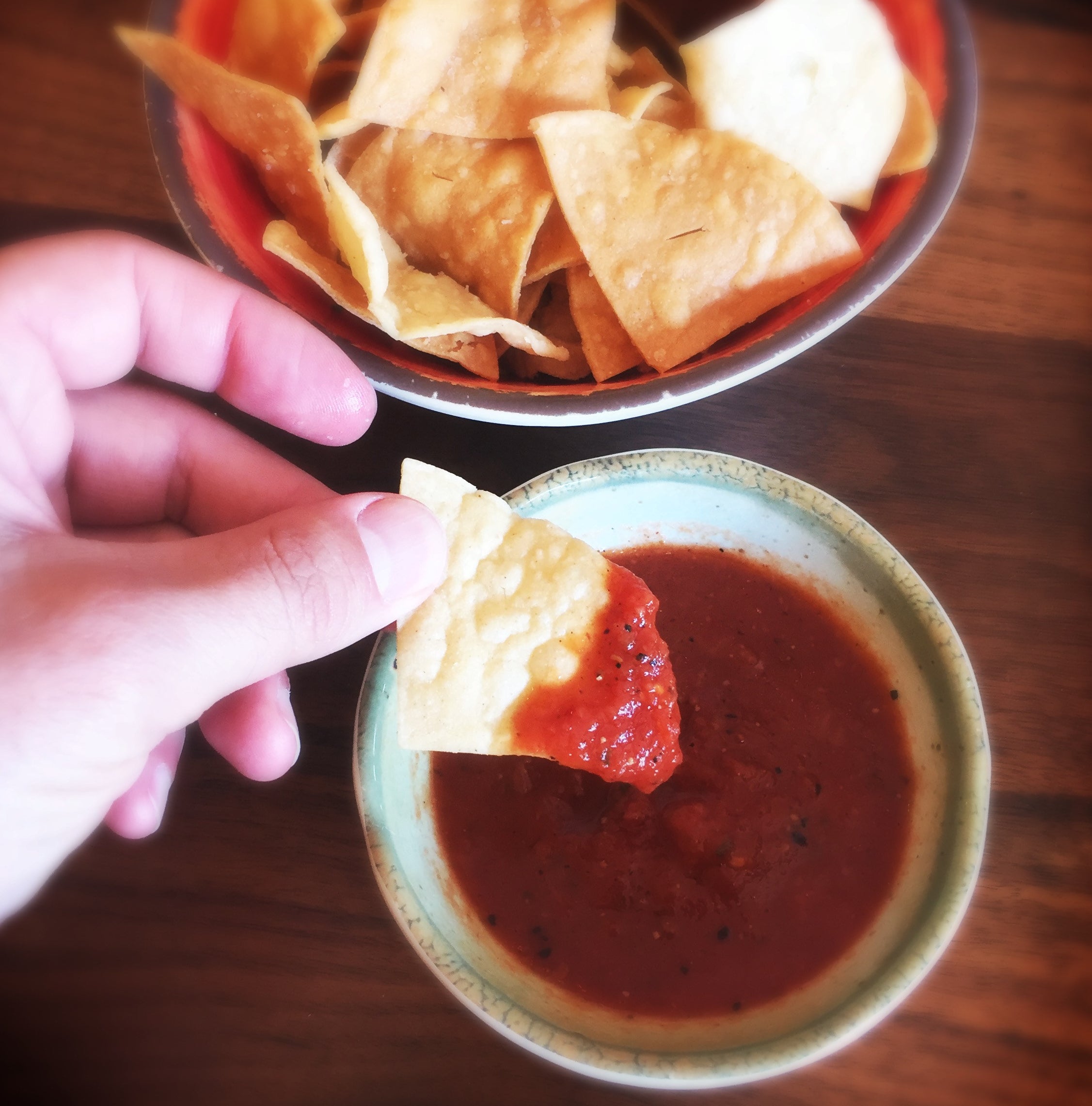 A hand dipping chips into salsa.