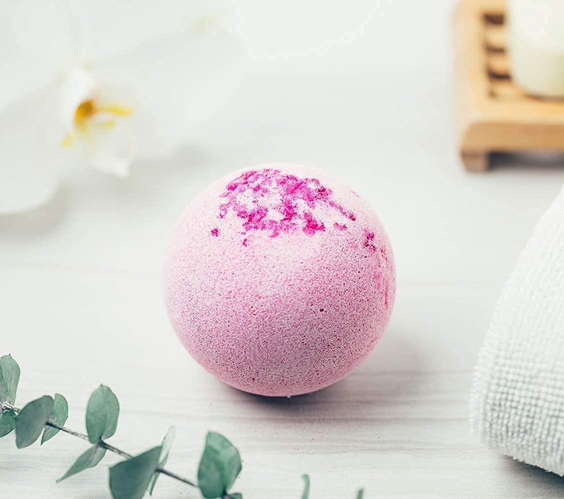 a bath bomb next to a folded towel and a stem of eucalyptus