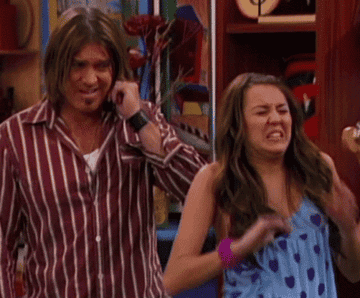 Miley and Billy Ray Cyrus plugging their ears with their hands.