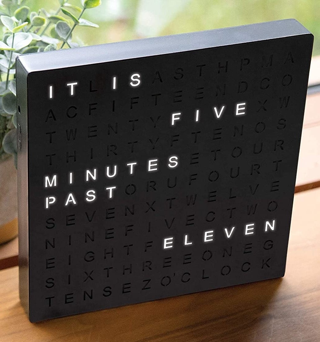 The clock in front of a plant on a wood table