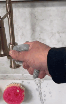 video of person wetting the sponge and using it to clean above a fridge