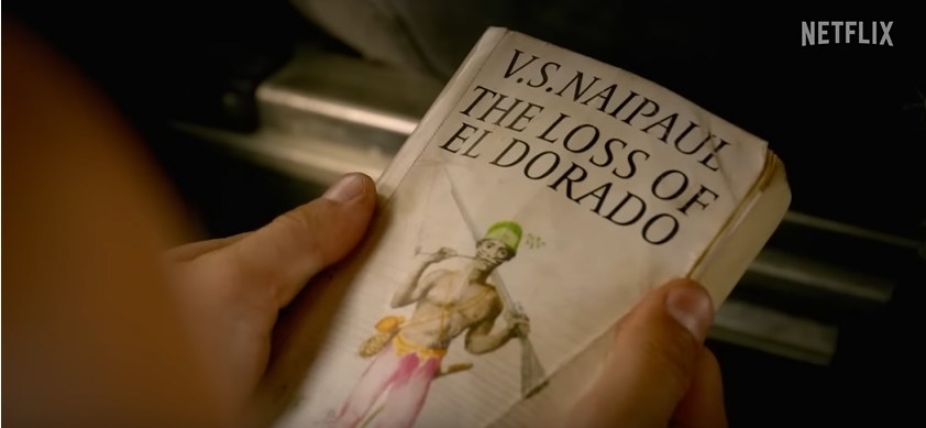 someone out of frame holding a book titled &quot;V S Naipaul the Loss of El Dorado&quot;