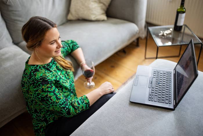 A woman with a glass of wine in her hand in front of her laptop