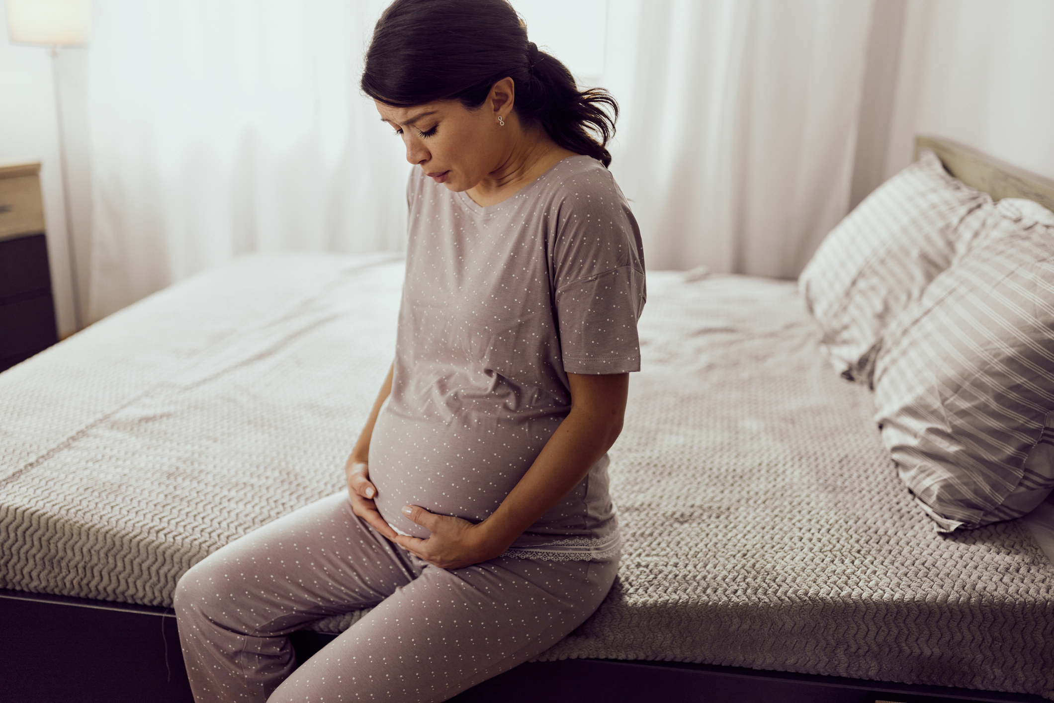 A pregnant woman sitting on her bed