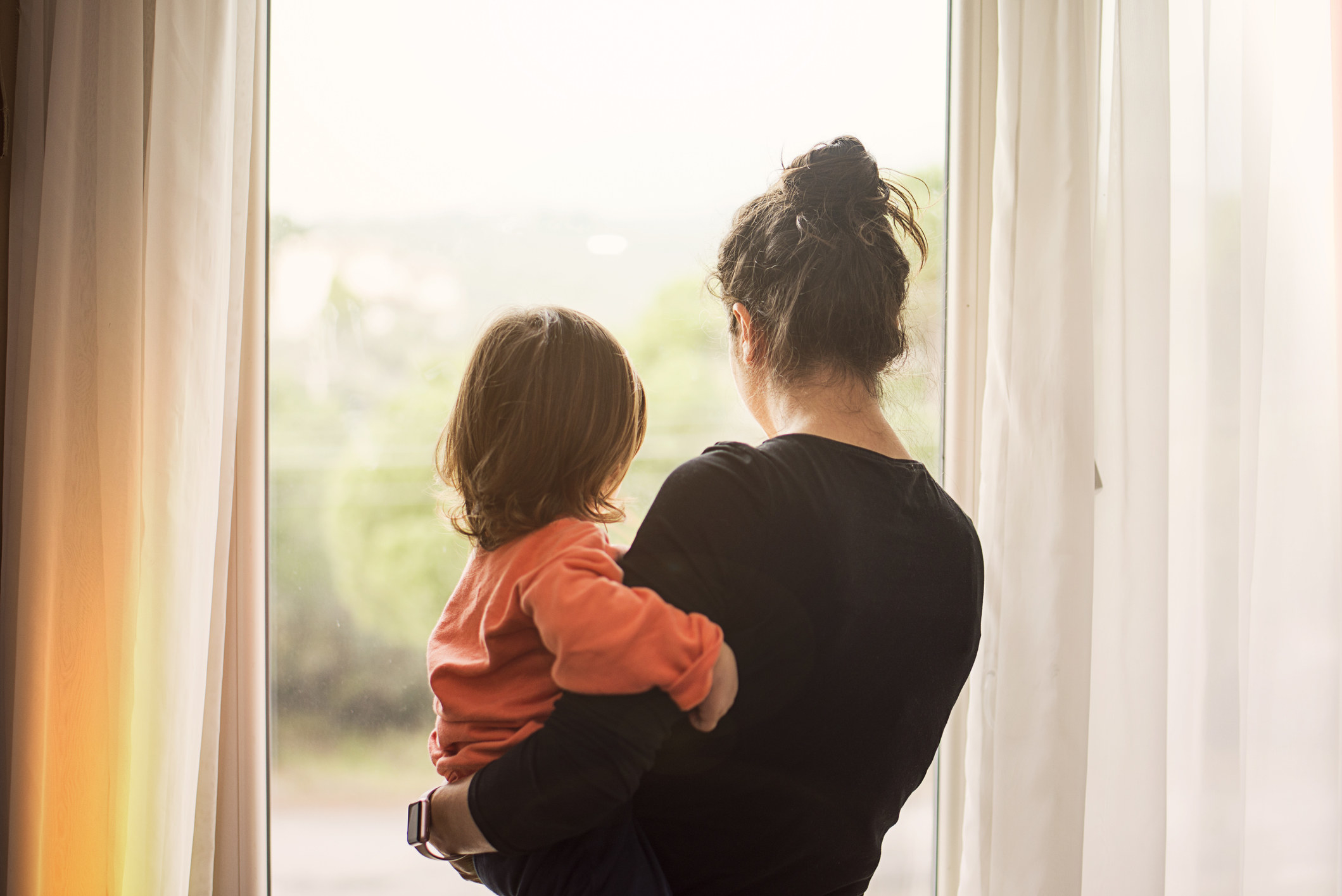 A mom holding her baby while looking out the window