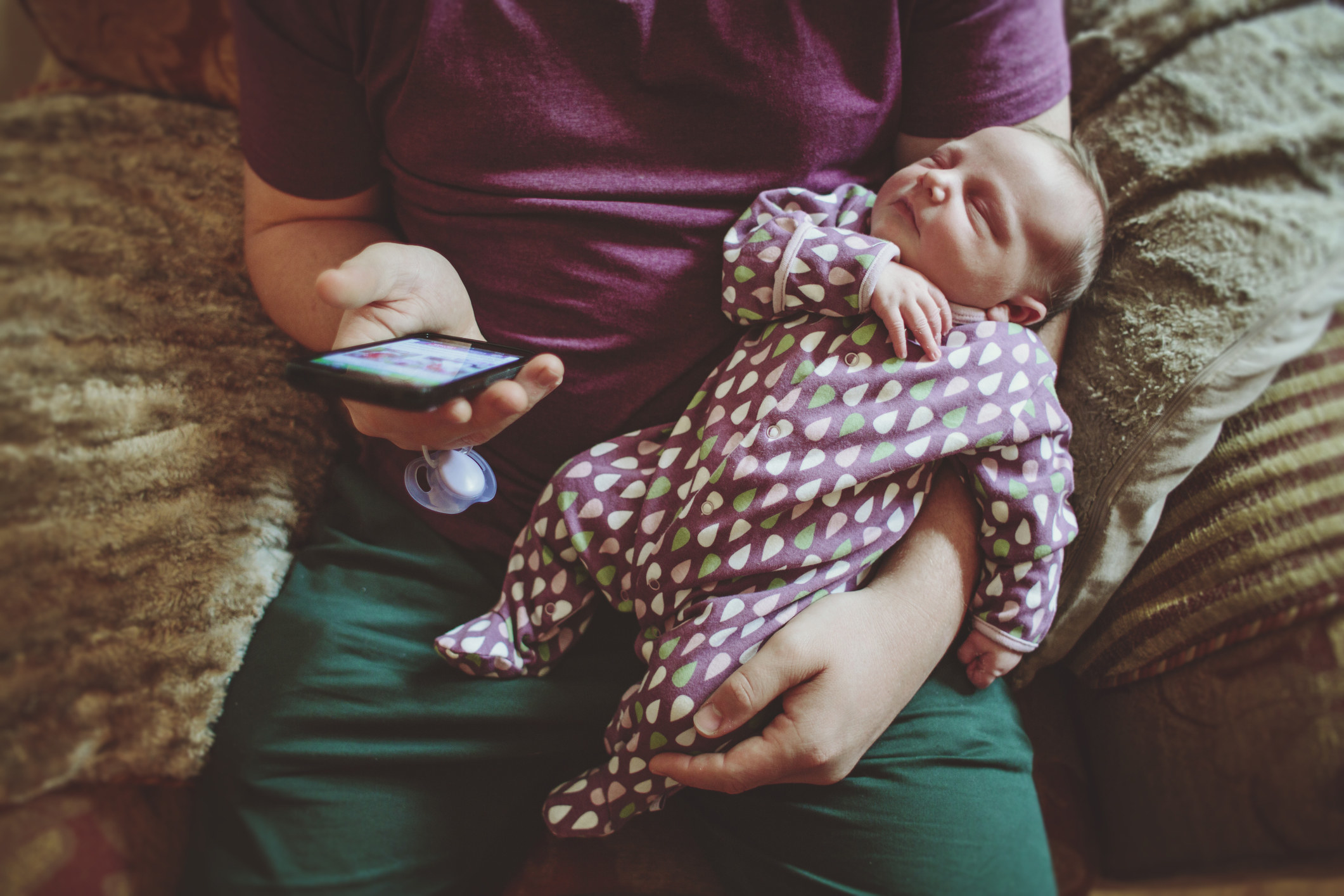 A parent holding their baby and scrolling on their phone