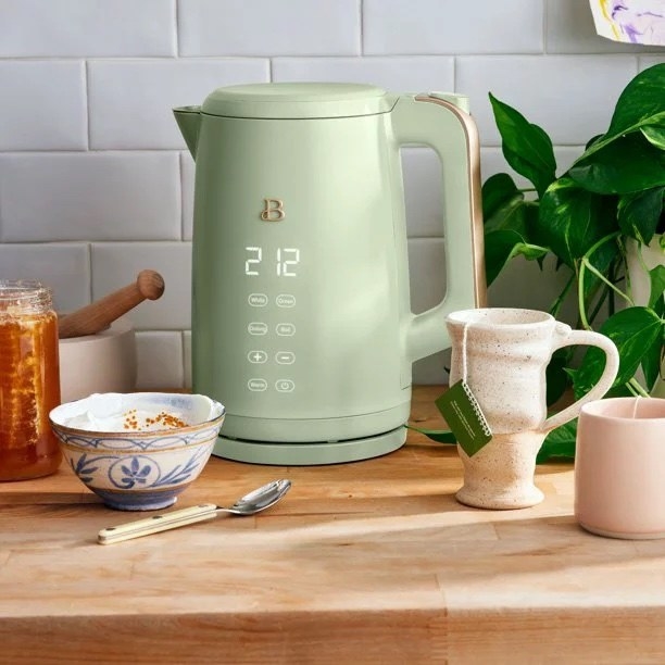a sage green electric kettle on a wooden table next to a mug