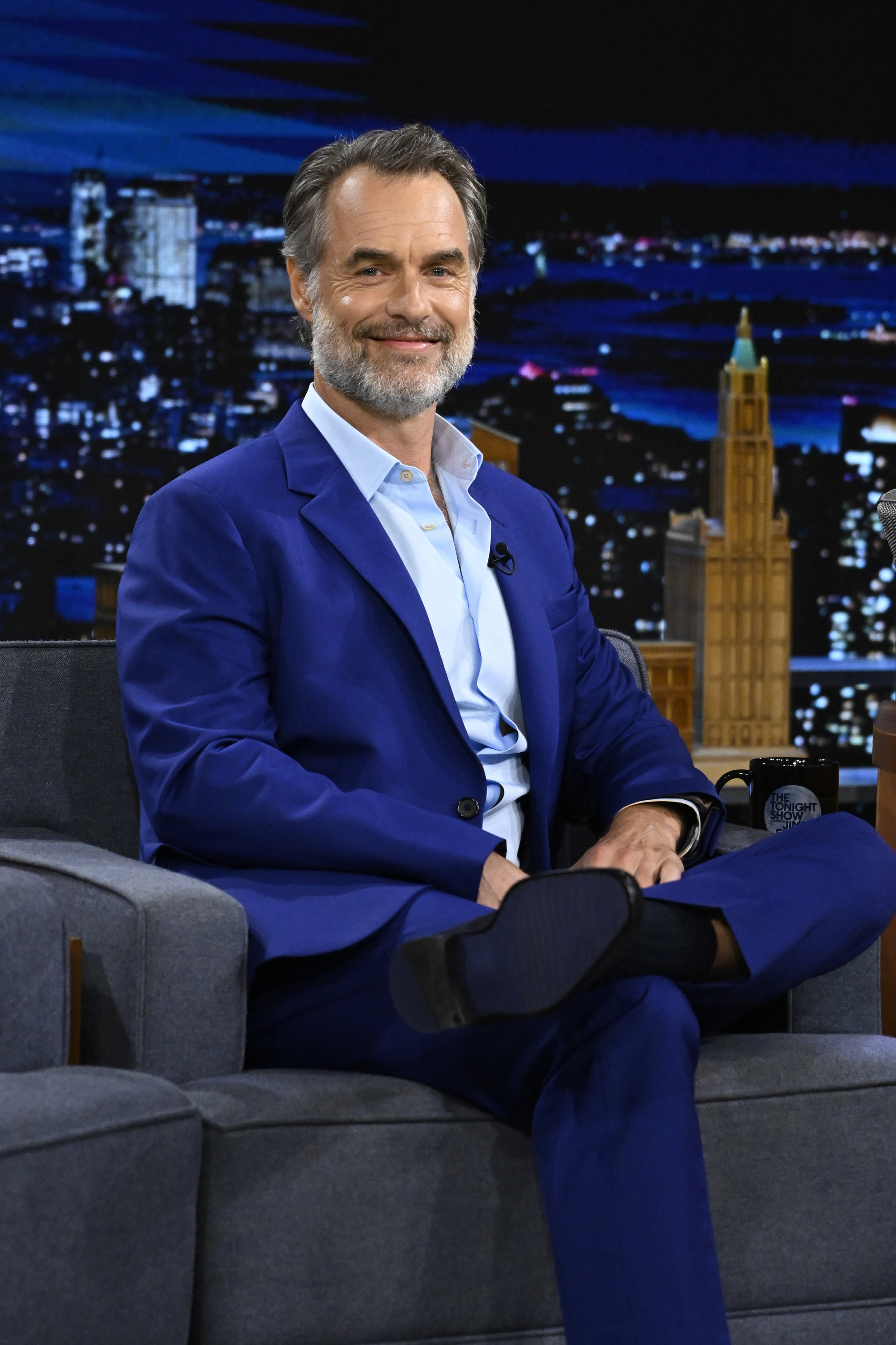 Murray Bartlett smiles as he sits onstage during a late-night TV show interview