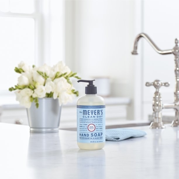 a blue and clear bottle of Mrs. Meyer&#x27;s Clean Day Rain Water Hand Soap near a kitchen sink