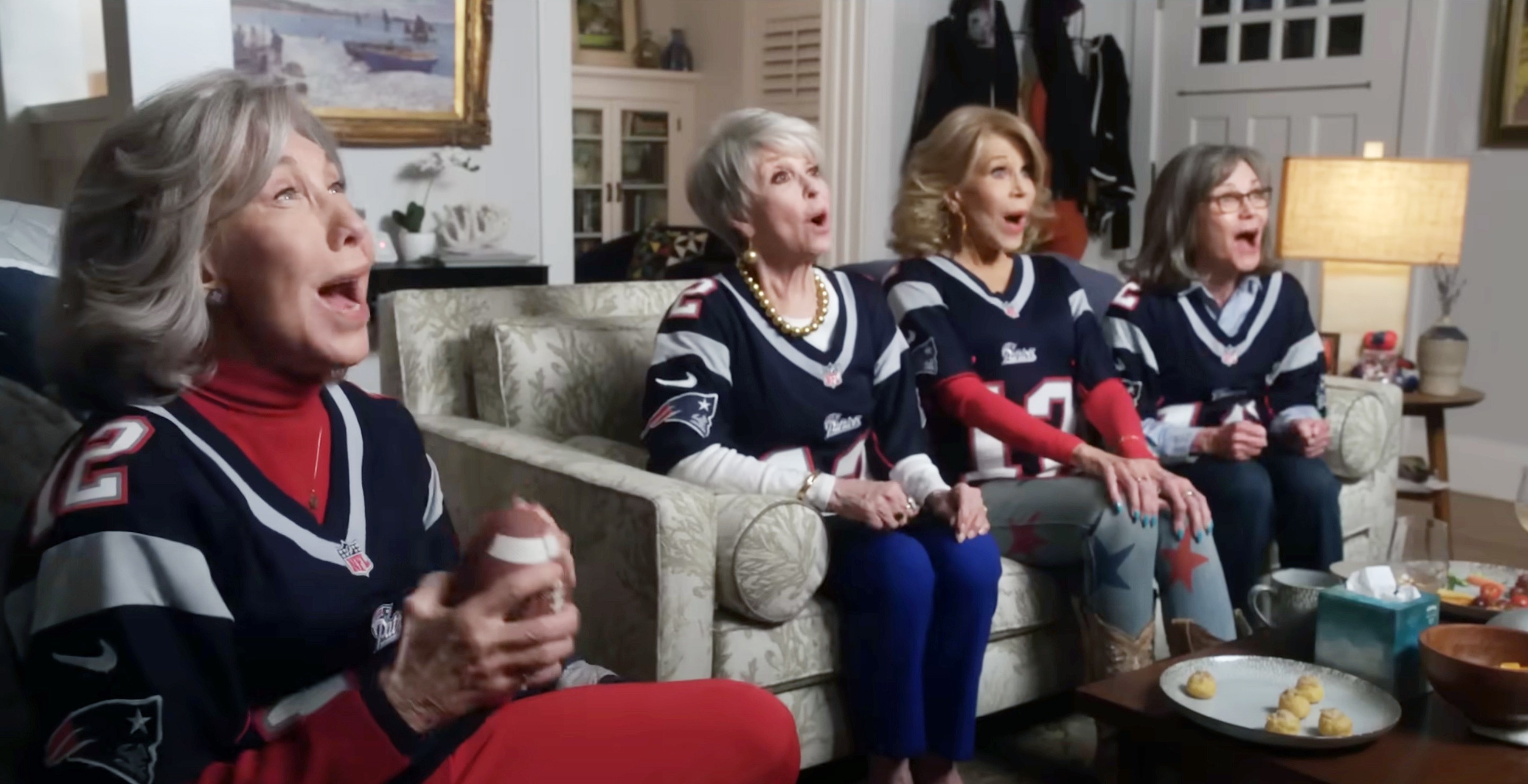 Lily, Rita, Jane, and Sally sit on the sofa at home watching the patriots