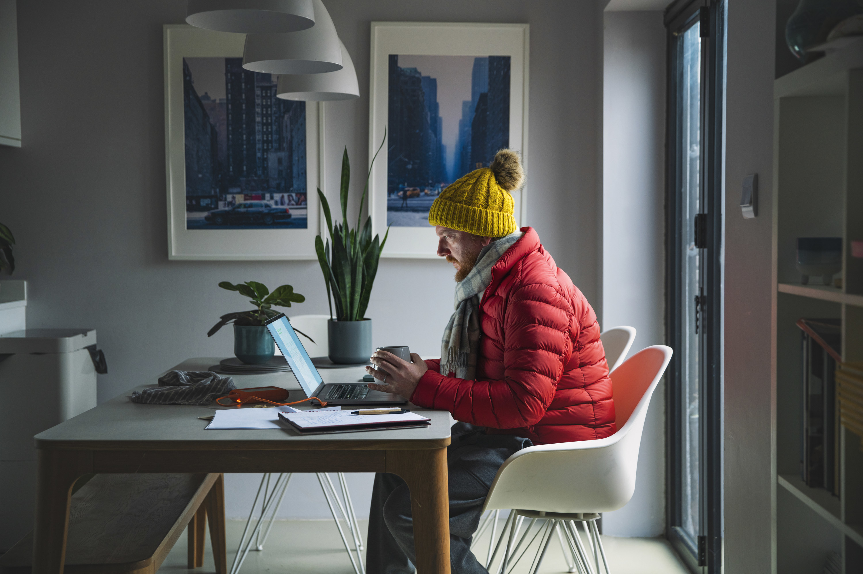 man wearing a parka scarf and knit hat to keep warm sitting in his home