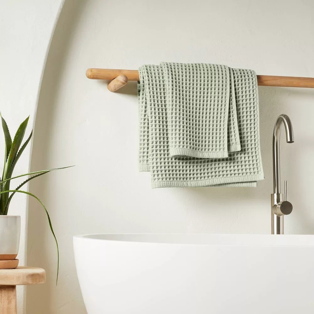 The green waffle pattern towel slung on a bamboo hanging rack next to a white bathtub