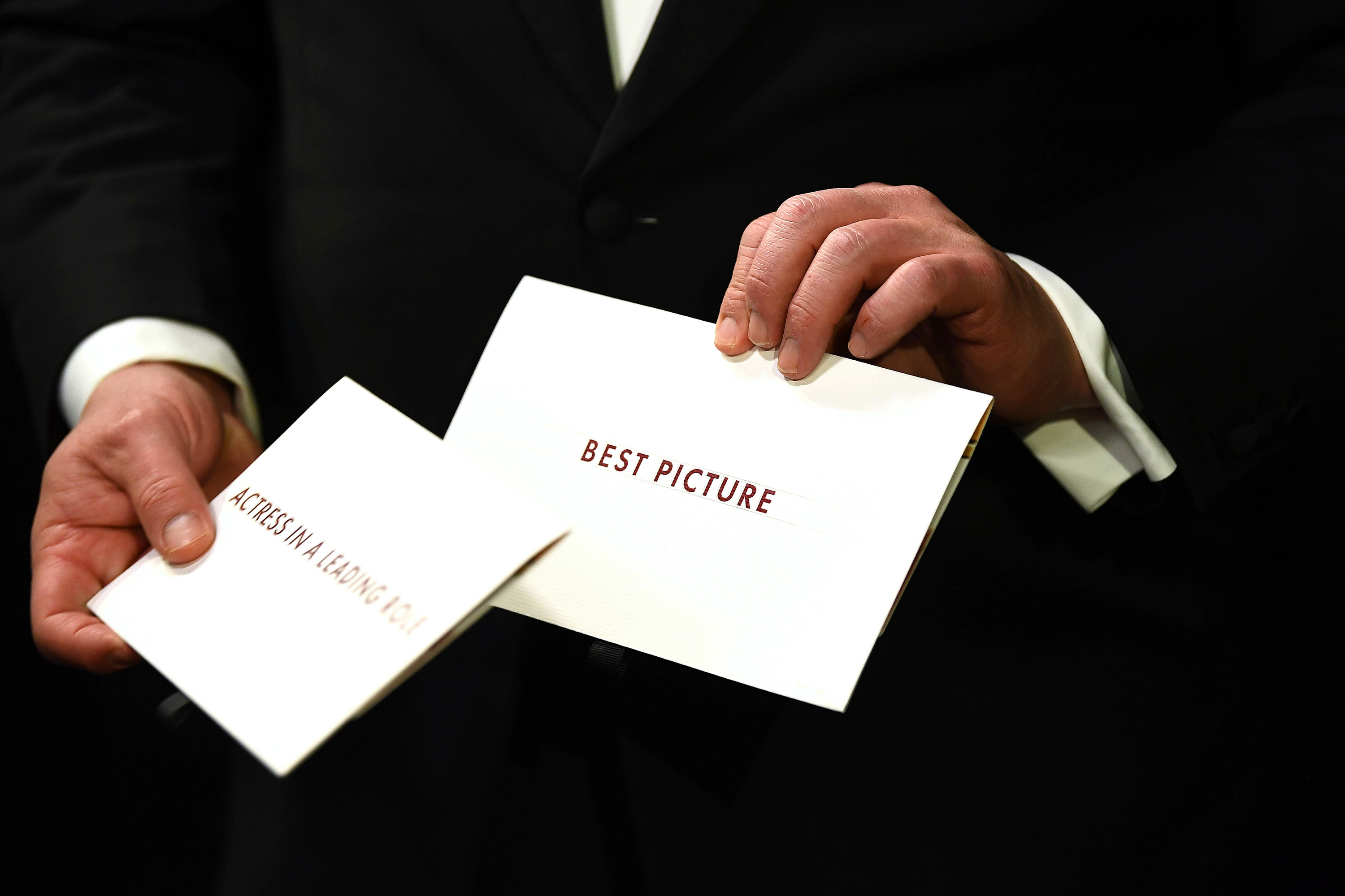 A pair of hands holding white envelopes for Best Picture and Best Actress awards